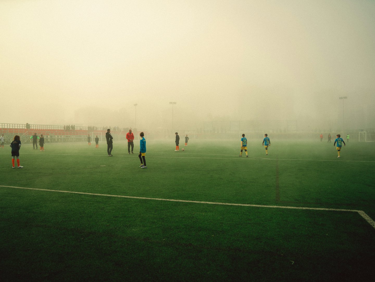Soccer players and coaches practice on a foggy turf field.
