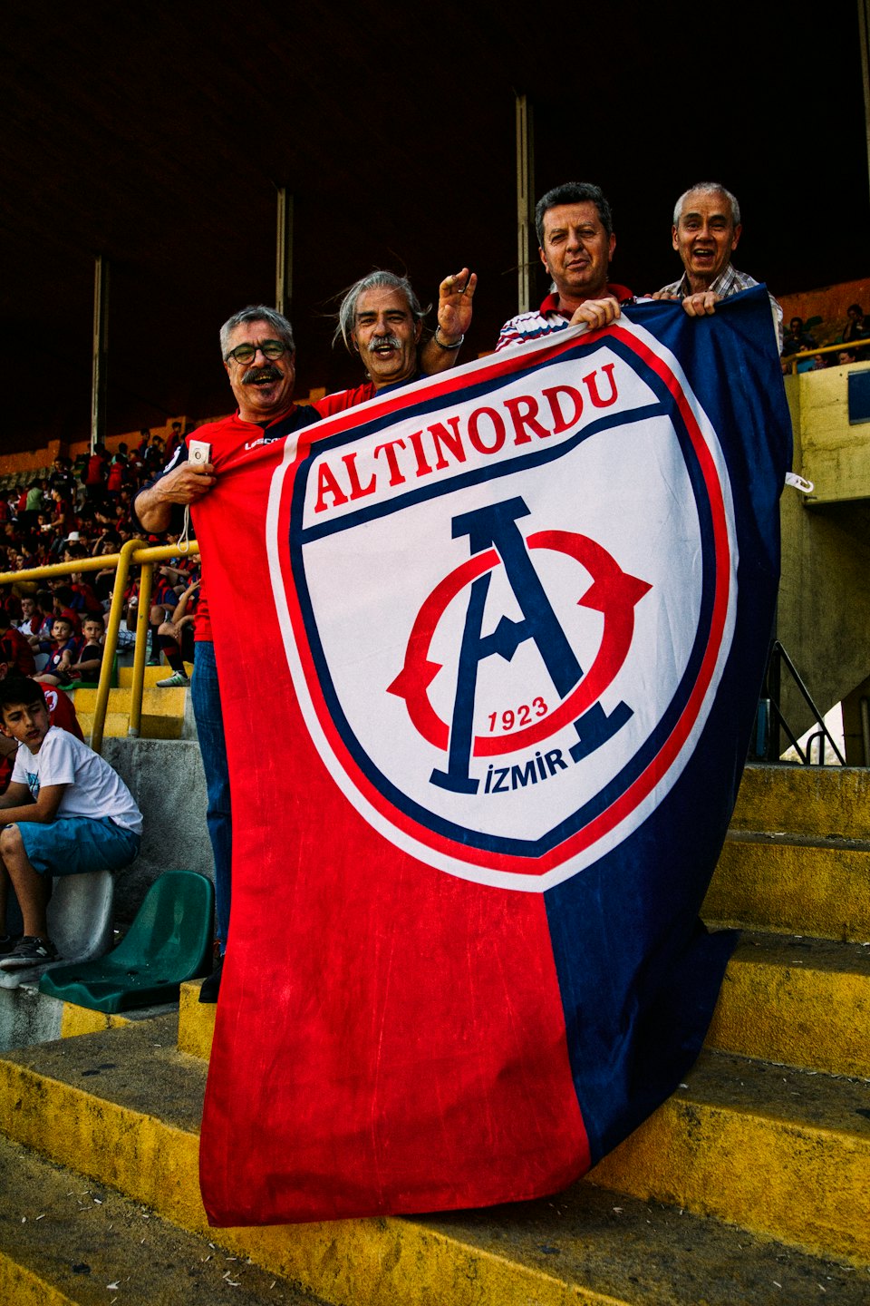 Four men holding a large football club flag on stadium steps.