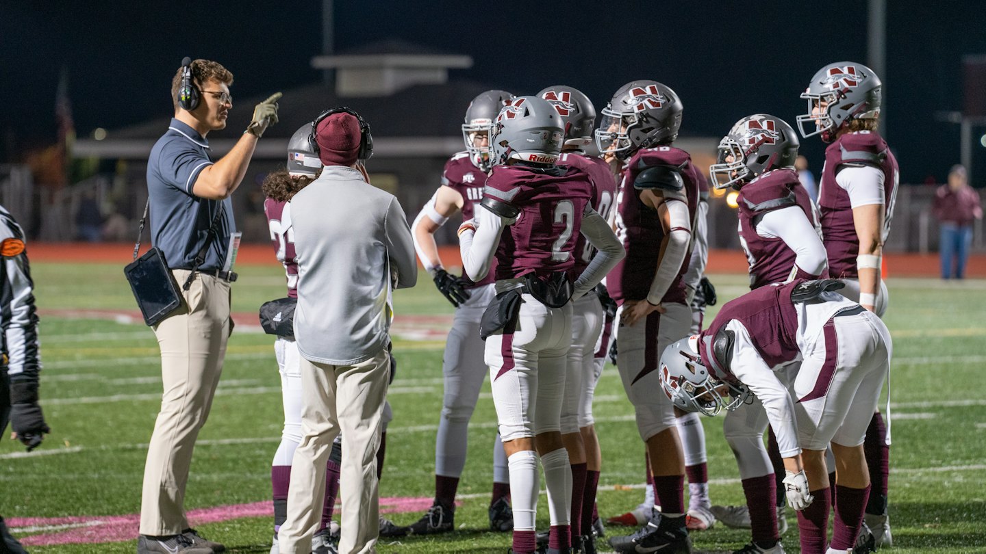 A football coach instructs players in a huddle on the field.