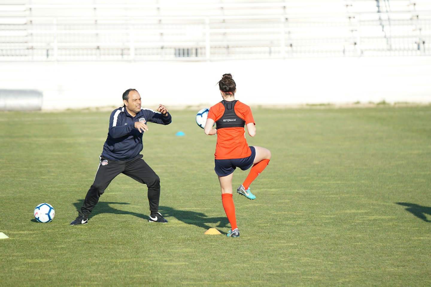 A soccer coach instructs a player practicing on a grass field.