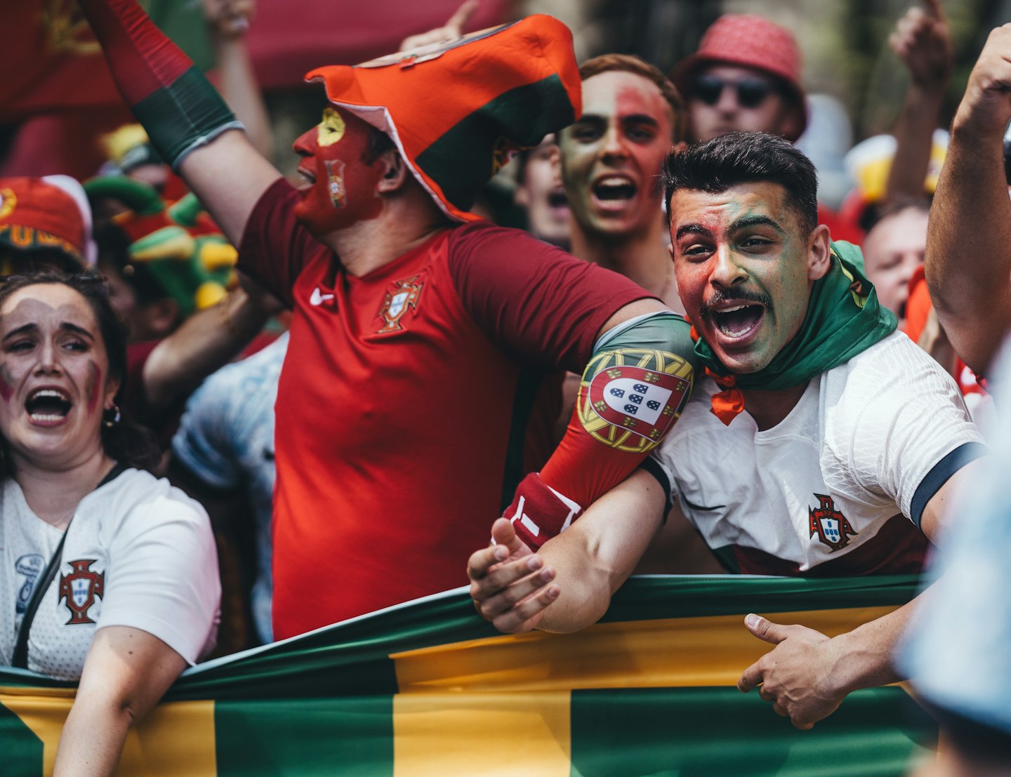 Football fans in Portugal jerseys cheer while holding a banner.