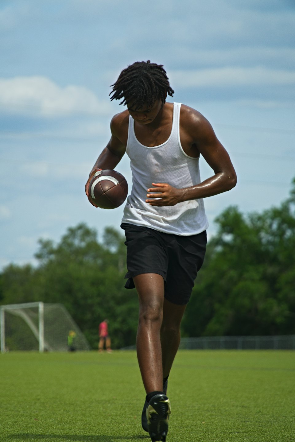 Athlete walking across a sports field holding a football.