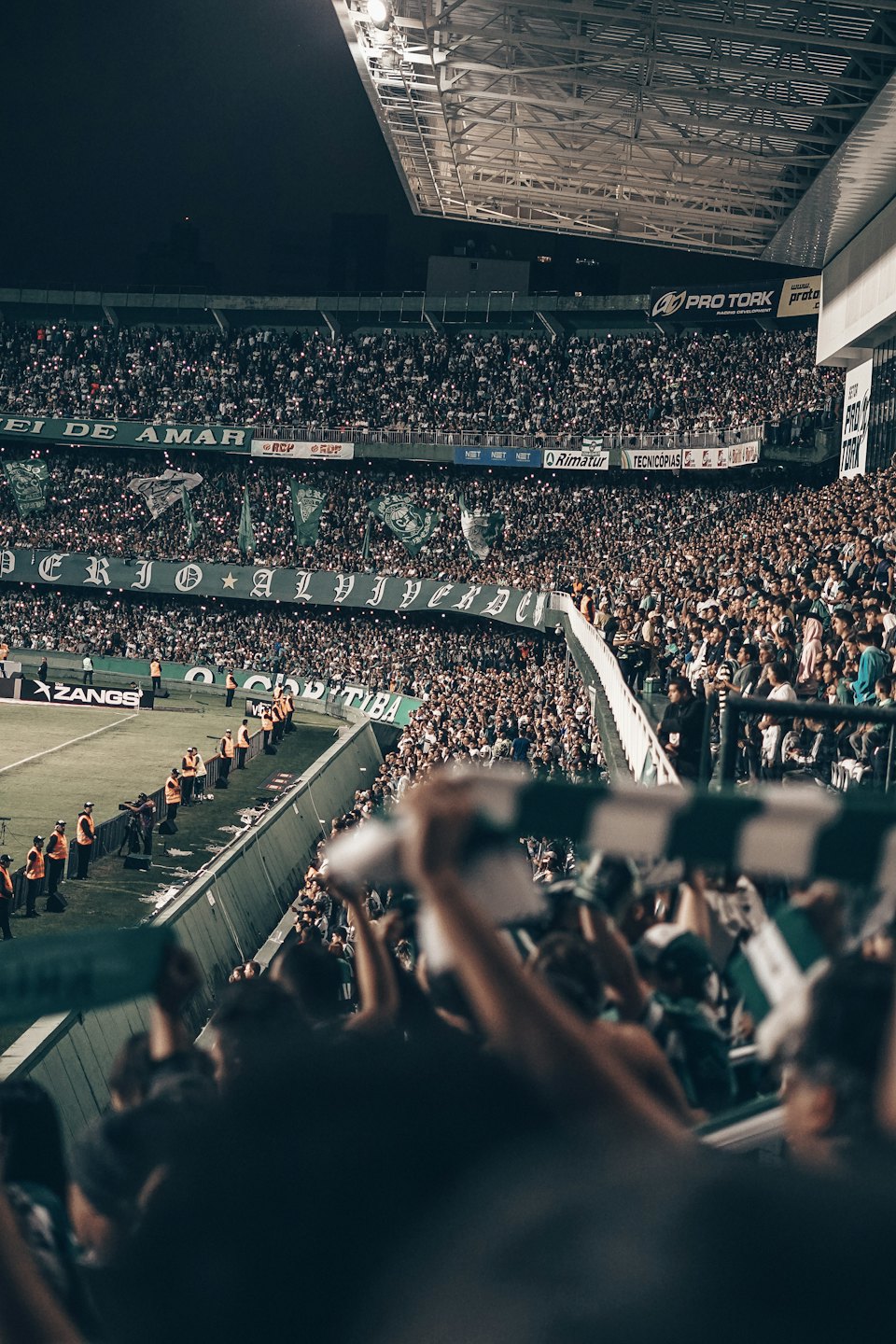Soccer fans cheer in stadium stands during a night game.