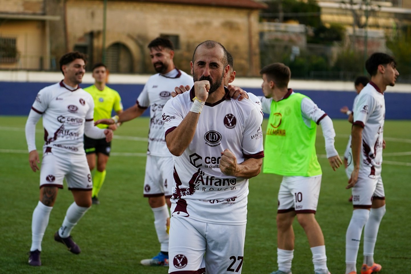 Soccer players in white and maroon uniforms celebrate a victory on turf.