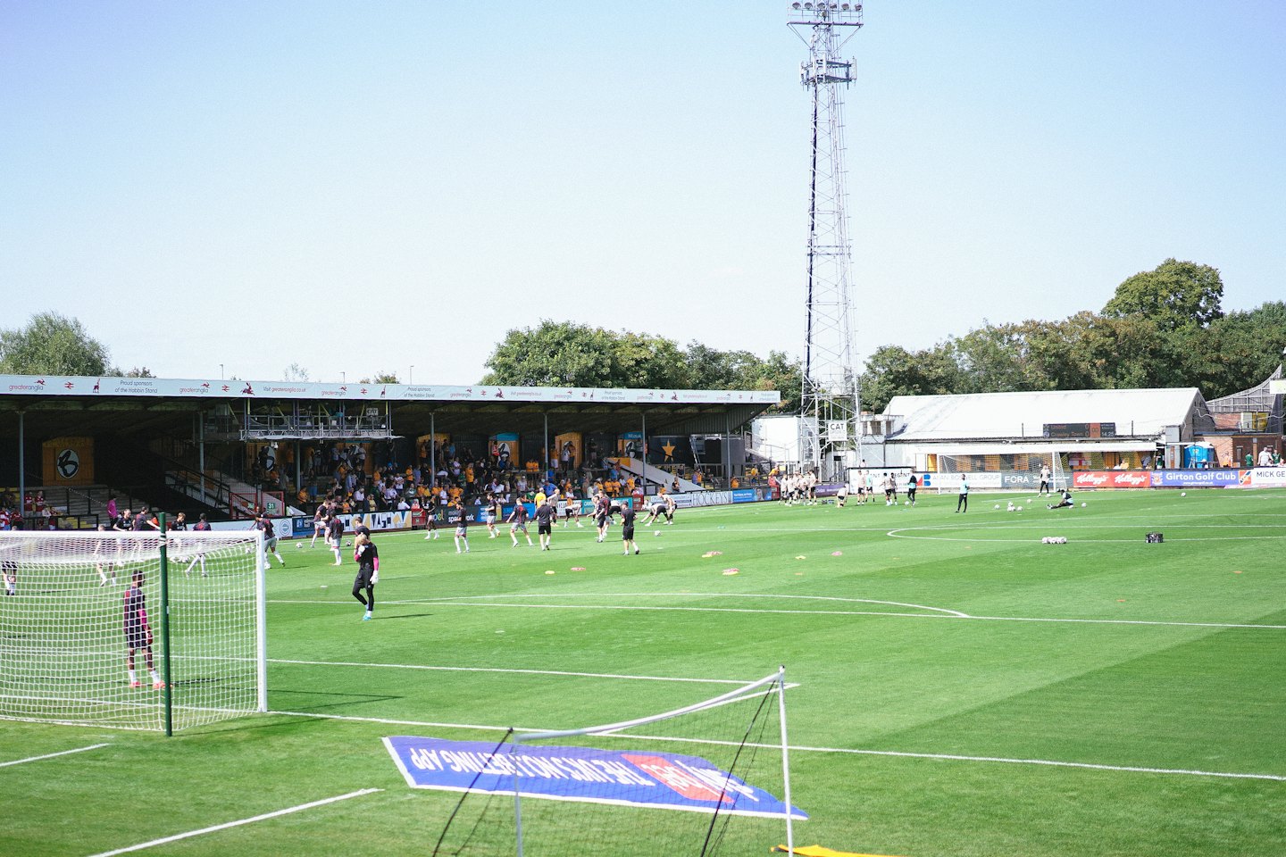 Football players train on a grassy stadium field before spectators.